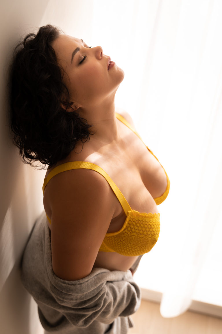 Femme en lingerie jaune, les yeux fermés, contre un mur baigné de soleil