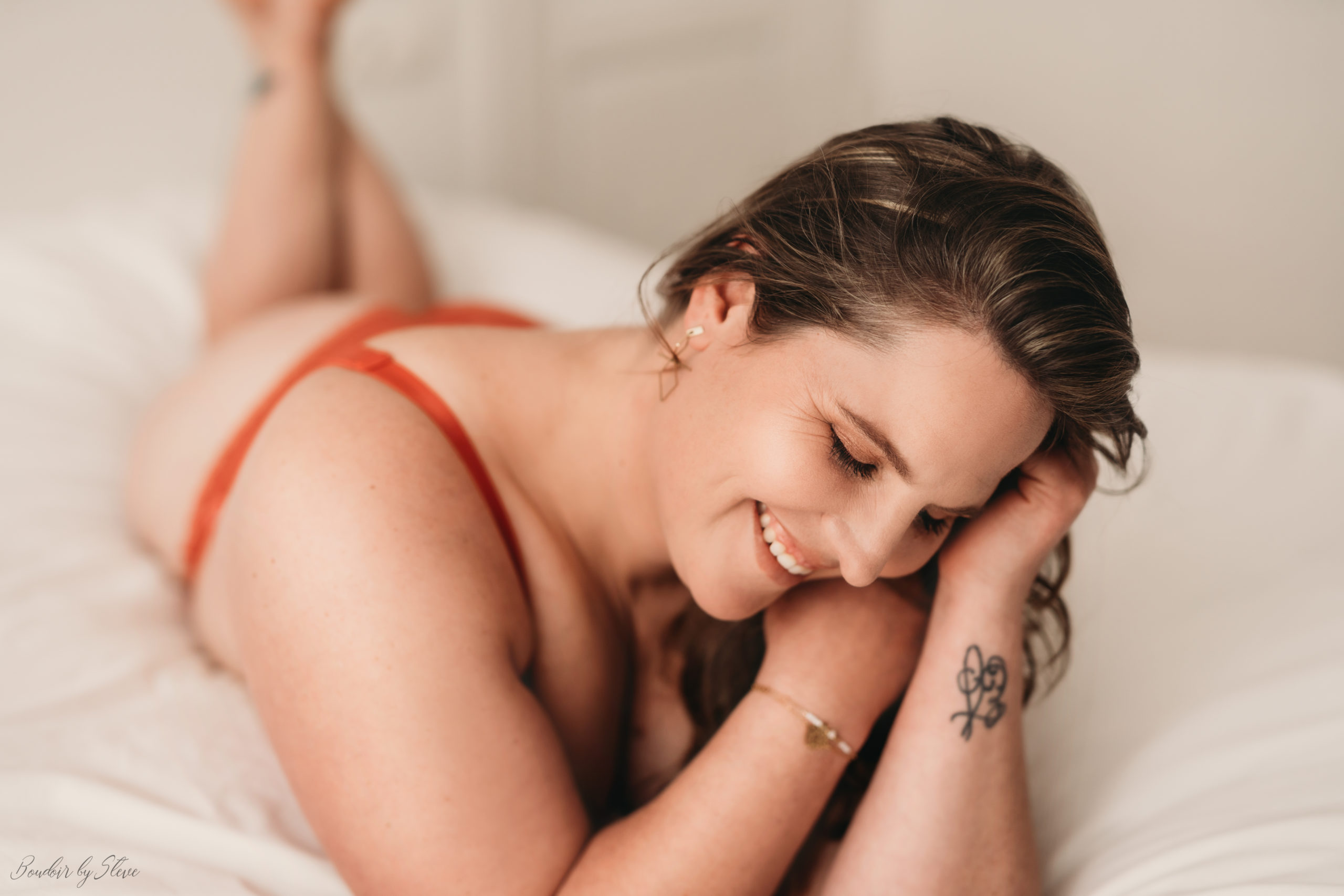 Smiling woman in red lingerie on a bed, boudoir photography in Belgium