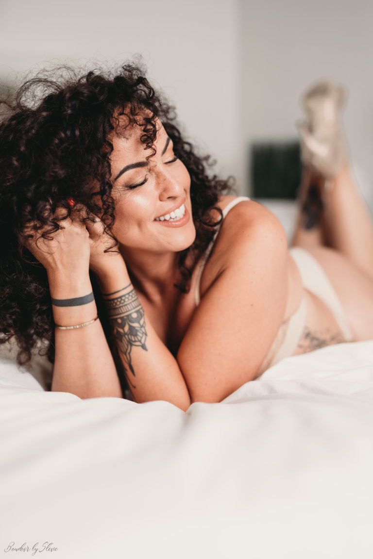 Femme aux cheveux bouclés, souriante, allongée sur un lit blanc