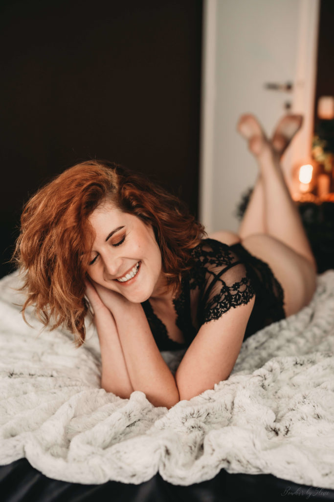 Smiling red-haired woman in black lace lying on a white throw