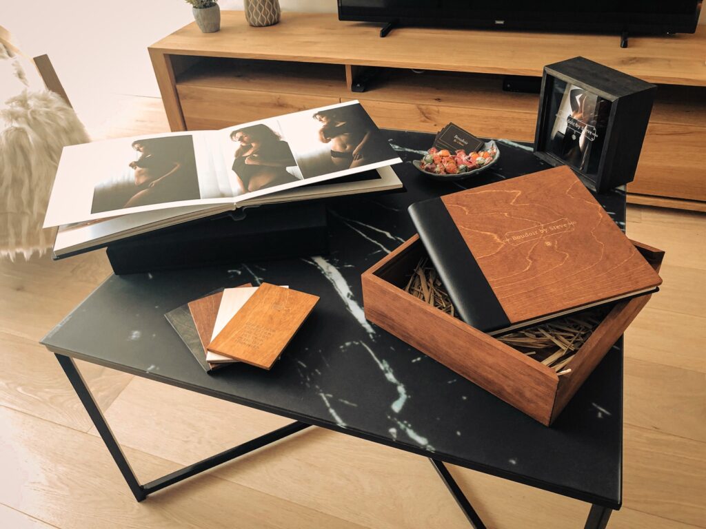 Album boudoir en bois gravé Boudoir by Steve, dans son coffret, à côté d'un album ouvert et d'échantillons de finitions