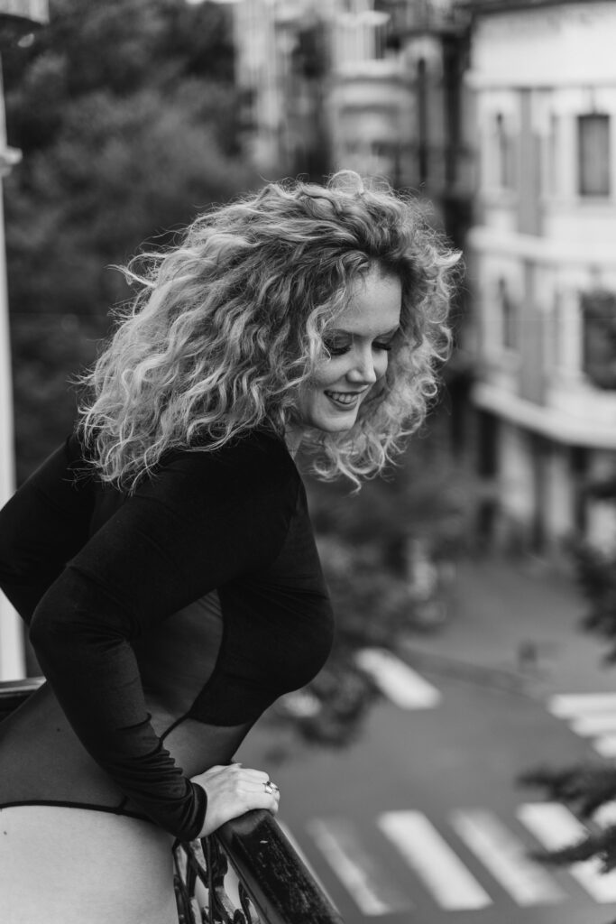 Black and white boudoir portrait of a smiling woman on a city balcony