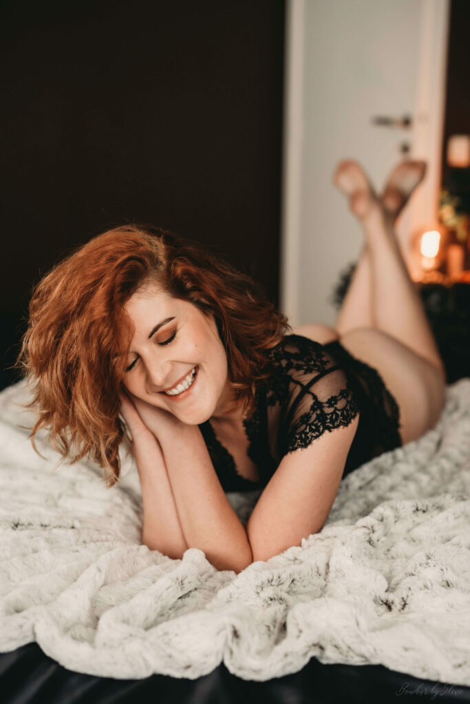 Femme rousse souriante en dentelle noire, allongée sur un plaid blanc