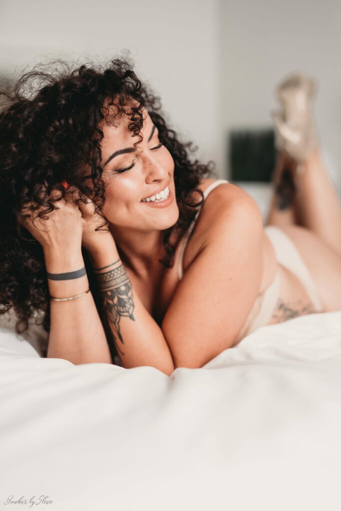 Femme aux cheveux bouclés, souriante, allongée sur un lit blanc